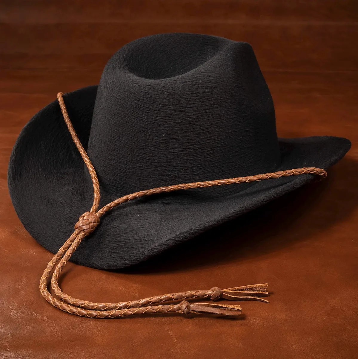 Black cowboy hat with a whiskey-colored braided leather stampede string, adjustable slider and leather tassel ends.